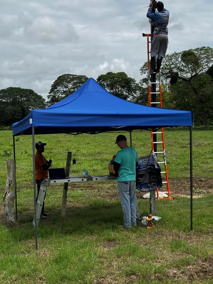 Técnicos de VSB instalando una cámara en un poste con una carpa y una escalera en el campo
